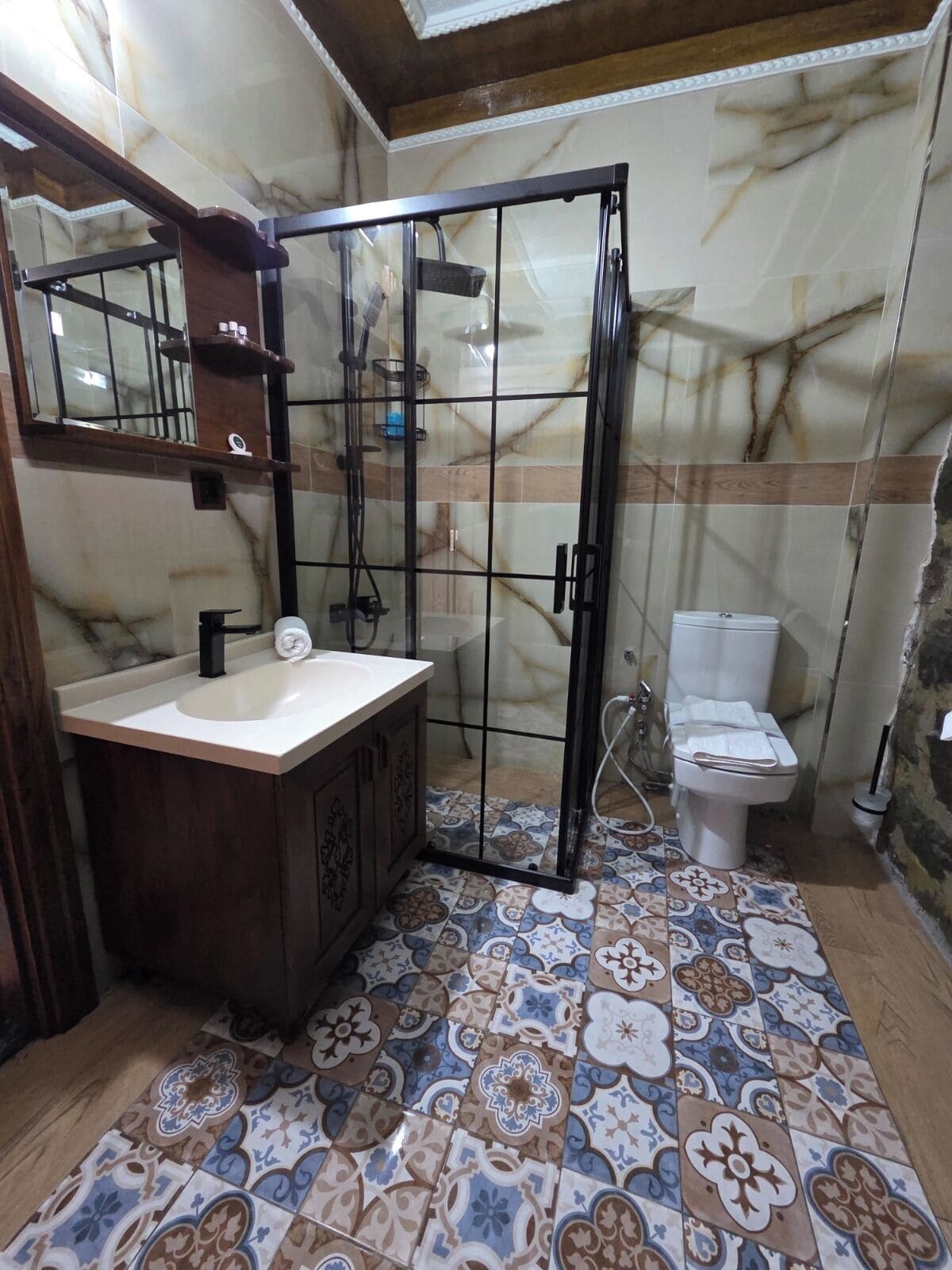 Een badkamer met een marmeren wand, een betegelde vloer, een wastafel met spiegel, een toilet en een douchecabine.