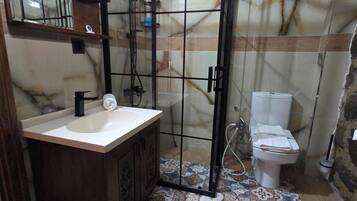 Un baño con pared de mármol, suelo de baldosas, lavamanos con espejo, inodoro y cabina de ducha.