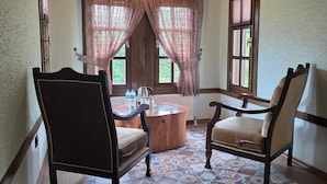 Una habitación con techo de madera, suelo de baldosas estampadas, una mesa de centro redonda, dos sillas y una ventana con cortinas.