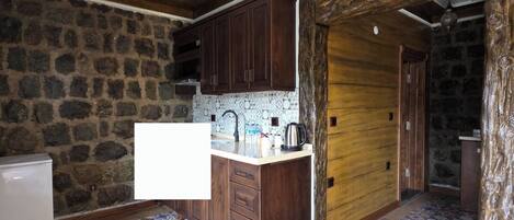 A kitchen with a stone wall, wooden cabinets, a tiled floor, and a wooden ceiling.