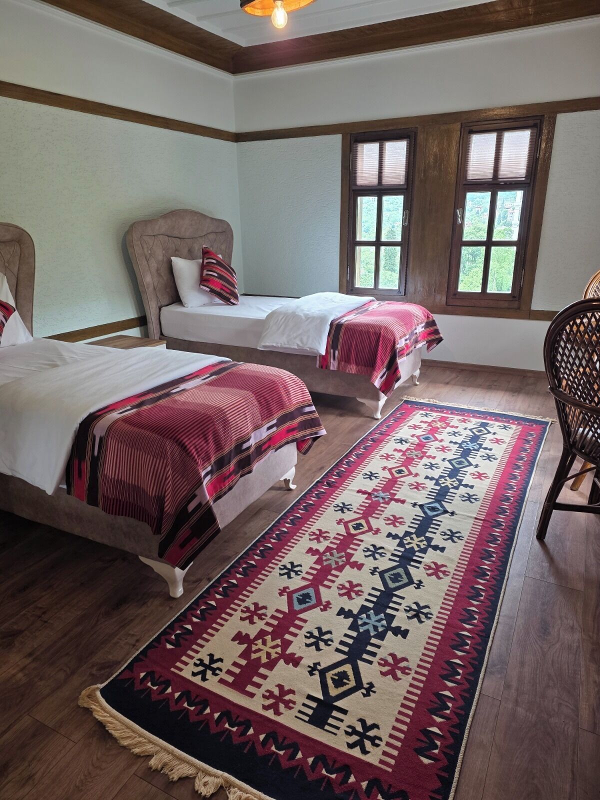 Une chambre d’hôtel avec deux lits, une grande moquette à motifs, un plancher en bois et une fenêtre avec des stores.