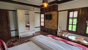 A bedroom with a large bed, a wardrobe, a stone accent wall, a television, and a window with blinds.