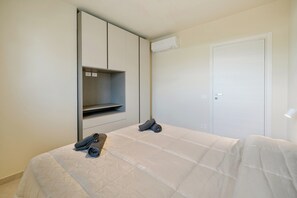A bedroom with a bed, a wardrobe, a built-in shelf, and an air conditioning unit. - Daulia, apartment in a villa near Soverato, on the Ionian coast of Calabria — open year-round (Marina di Davoli)