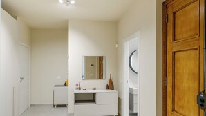 Um corredor com toucador branco, espelho e porta de madeira.