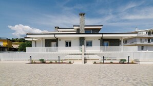 Uma casa moderna de dois andares, com cerca branca, chaminé central e calçada pavimentada.
