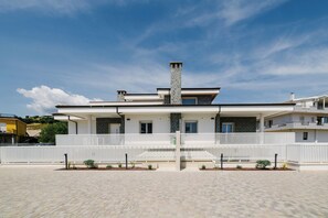 Ein modernes, zweistöckiges Haus mit weißem Zaun, einem zentralen Schornstein und einem gepflasterten Einfahrtsweg.