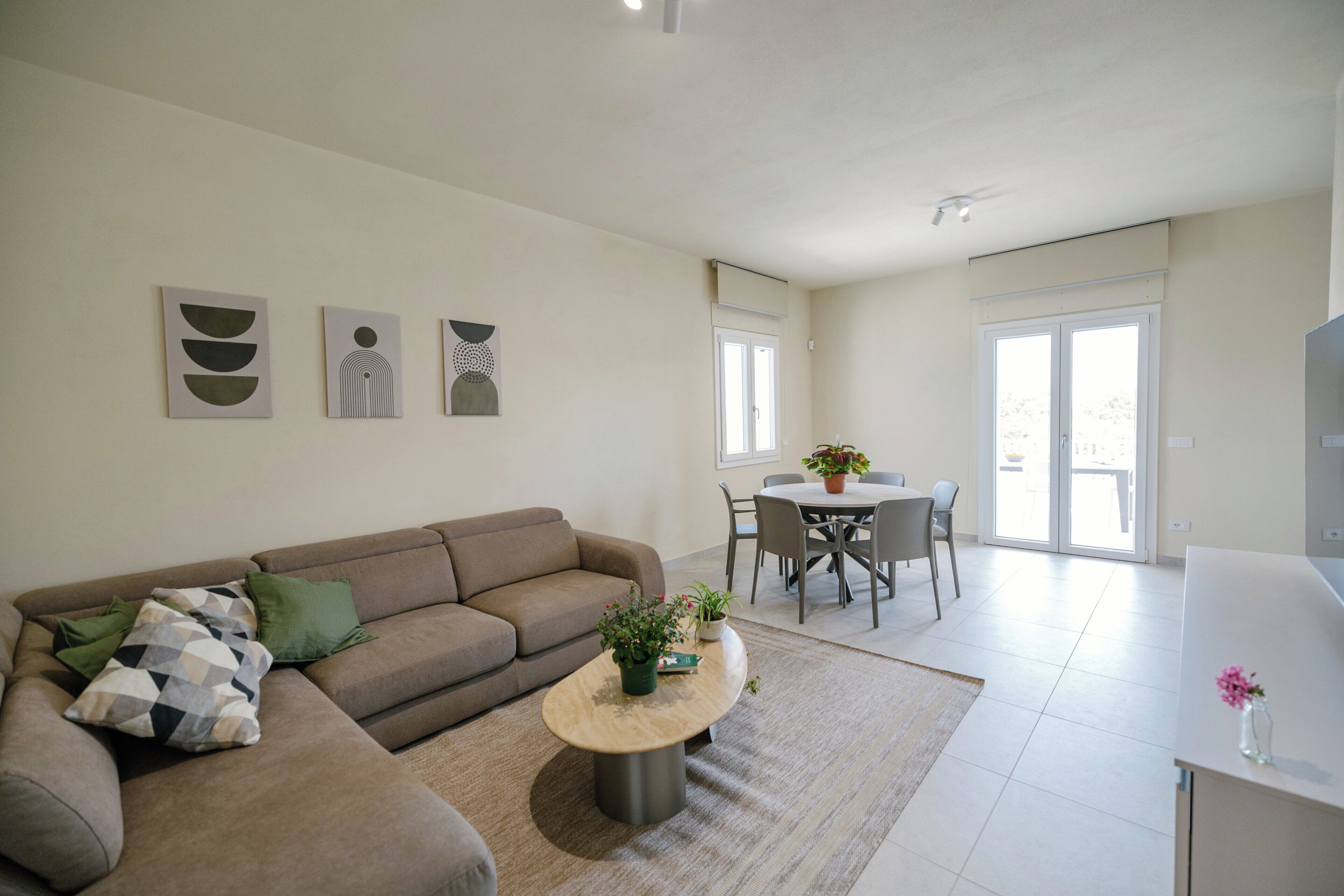 Ein Wohnzimmer mit einer Couch, einem Couchtisch mit einer Pflanze sowie einem Essbereich mit Stühlen und einem Tisch.