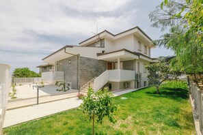 Ein modernes, zweistöckiges Haus mit Naturstein-Fassade, einem Balkon und einem gepflegten Rasen.