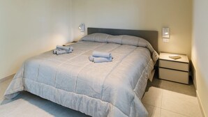 Quarto com cama, mesas de cabeceira e luminária no teto.