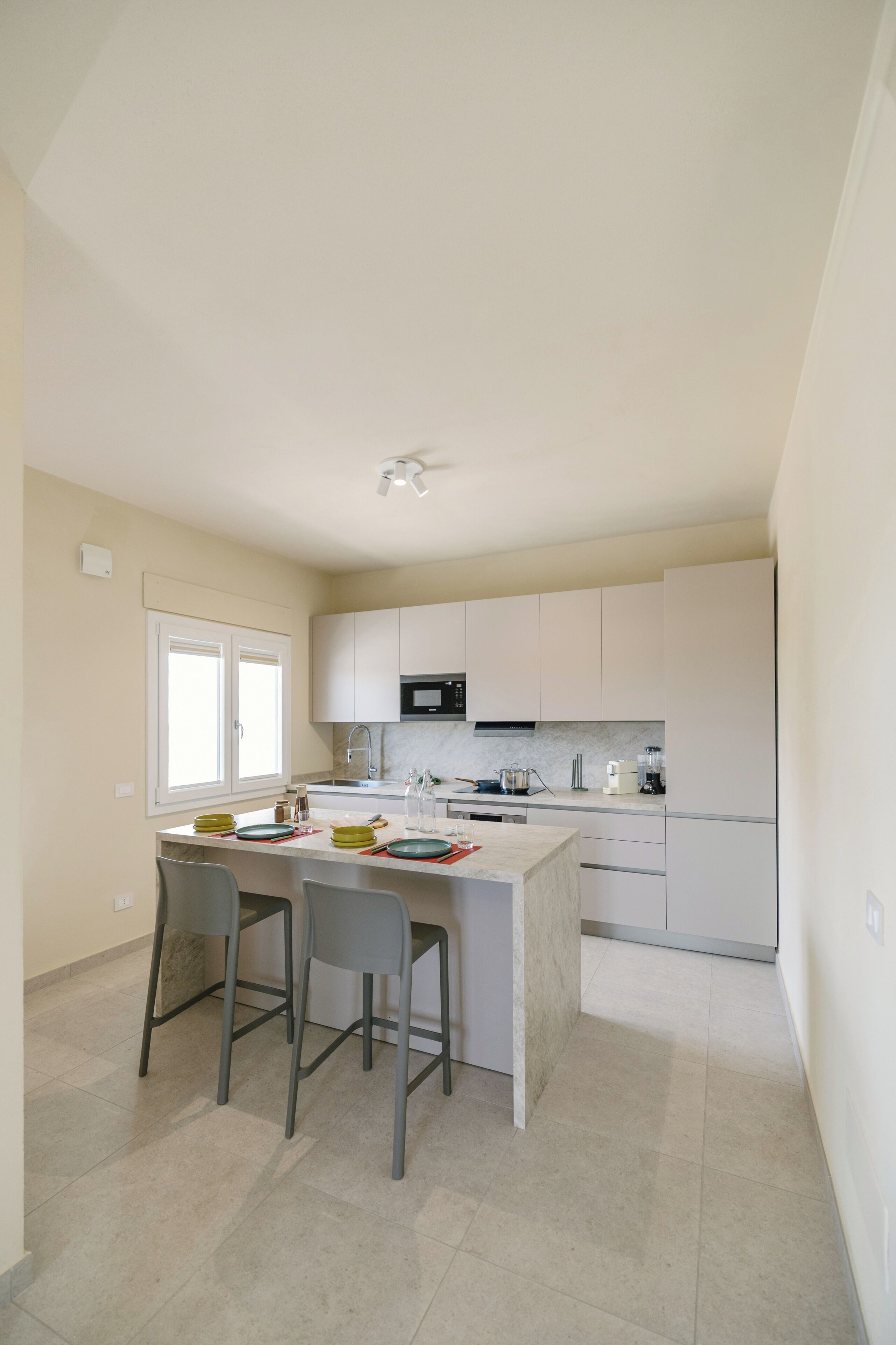 Una cocina moderna con armarios blancos, una isla central con taburetes de bar, microondas y un lavamanos.