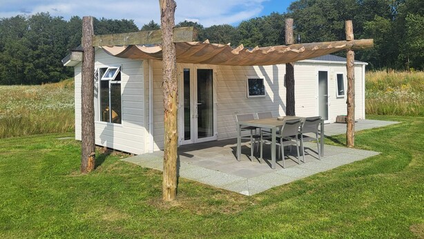 A small, single-story cabin with a patio area, a table and chairs, and a pergola structure. - Modern Pet-friendly Retreat in Limburg (Heythuysen)