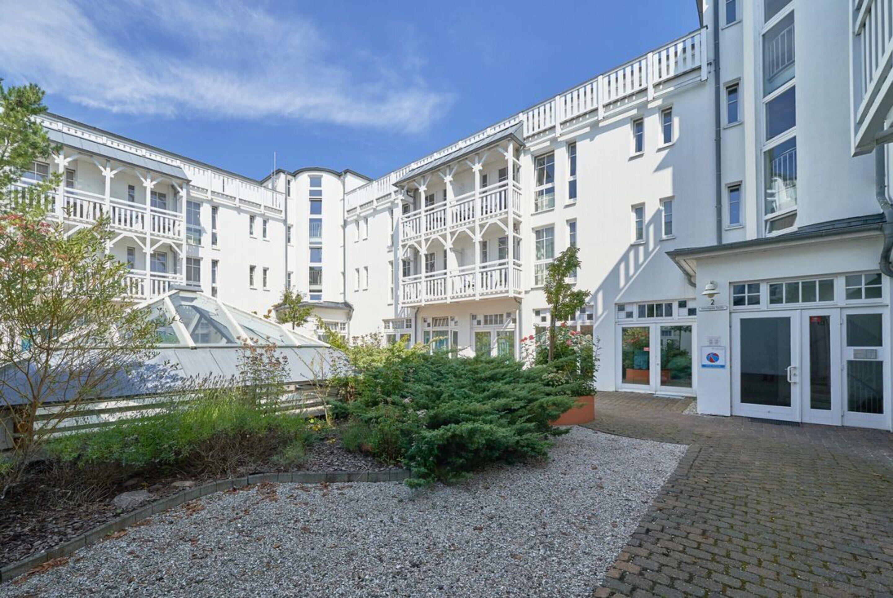 En bygning med flere etager, altaner, et drivhus og en grusgård.
