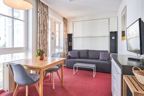 A modern living room with a sofa, a dining table with chairs, a TV, and a bookshelf. - Schone Ferienwohnung in Sellin mit Balkon (Sellin)