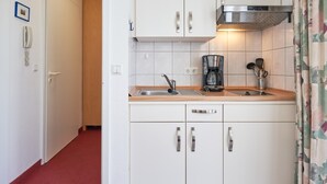 A compact kitchen with white cabinets, a stainless steel range hood, a coffee maker, and a sink. - Schone Ferienwohnung in Sellin mit Balkon (Sellin)