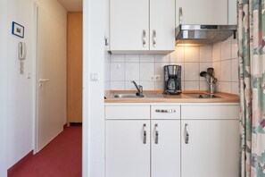 A compact kitchen with white cabinets, a stainless steel range hood, a coffee maker, and a sink. - Schone Ferienwohnung in Sellin mit Balkon (Sellin)
