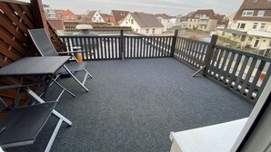 Un balcon donnant sur des immeubles d’habitation, une clôture en bois et deux fauteuils de jardin.