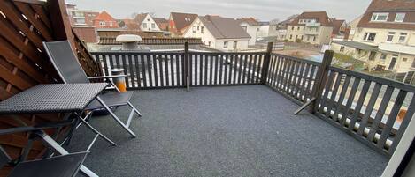 Un balcon donnant sur des immeubles d’habitation, une clôture en bois et deux fauteuils de jardin.
