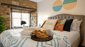A bed with a headboard, a window with a view, and a wall with abstract art. - Historic Flat Cotswolds 2BD Walk in Shower Central (Cirencester)