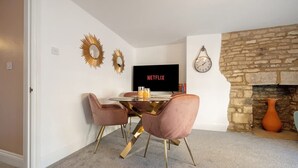 A room with a stone fireplace, a dining table with chairs, a television displaying 'NETFLIX,' and decorative wall mirrors. - Historic Flat Cotswolds 2BD Walk in Shower Central (Cirencester)