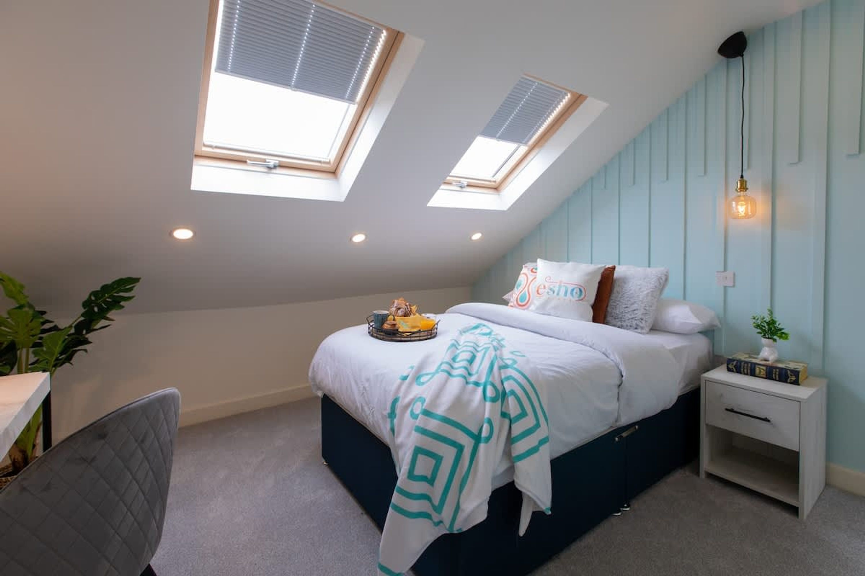 A bedroom with a bed, skylights, a bedside table, and a chair.