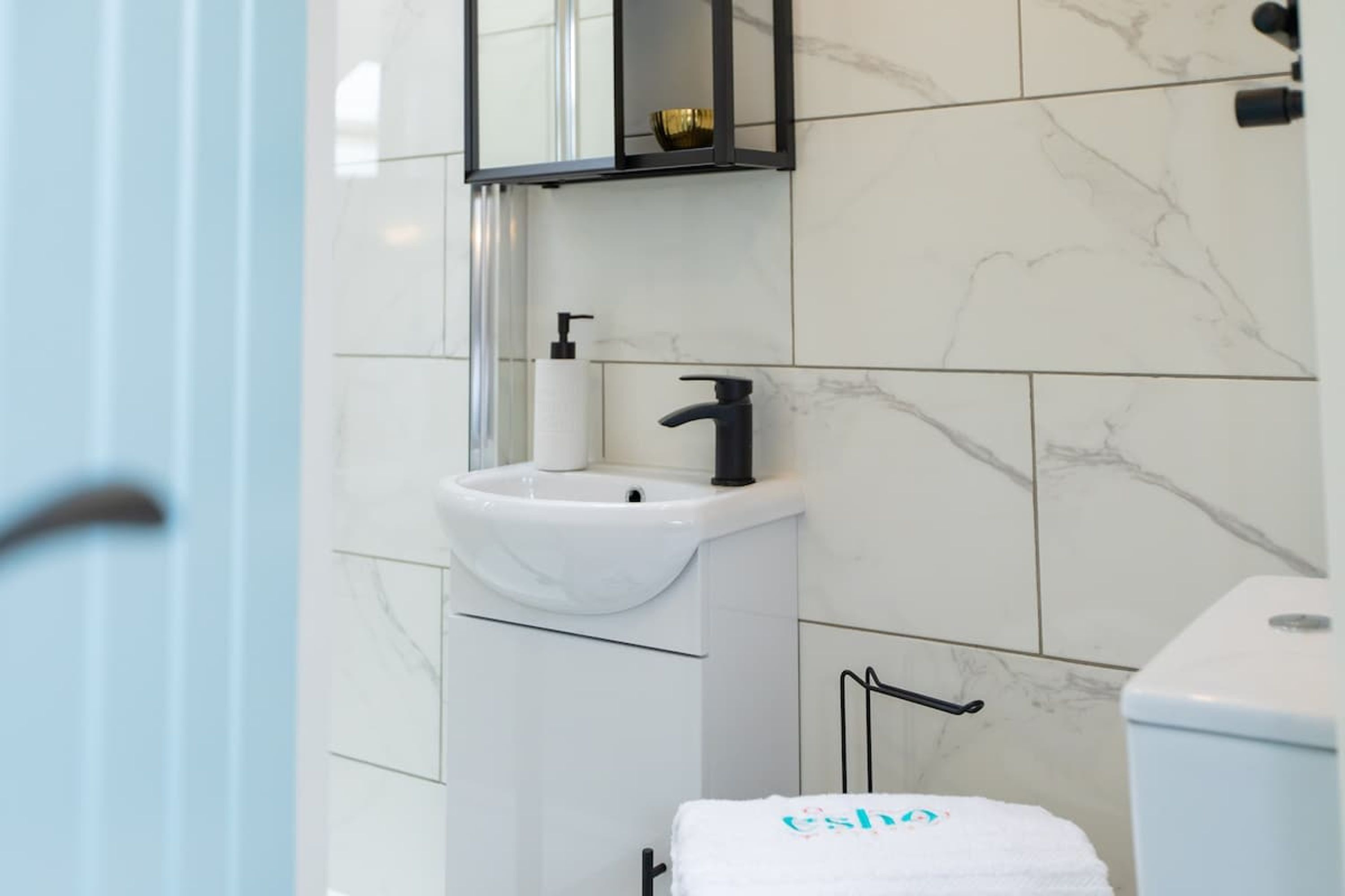 A bathroom with a white sink, black faucet, and a towel with 'ESLA' on it.
