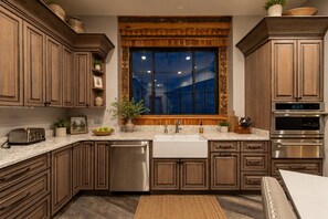 A kitchen with wooden cabinets, a stainless steel dishwasher, an oven, and a window with a view. - Bear Necessities Lodge: 16,000 SqFt Estate | Indoor Pool, Pickleball, Theater!!! (Sevierville)