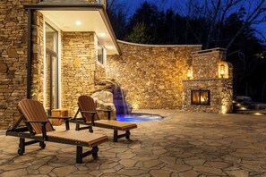 A stone building with a stone patio, outdoor seating, a waterfall feature, and a fireplace. - Bear Necessities Lodge: 16,000 SqFt Estate | Indoor Pool, Pickleball, Theater!!! (Sevierville)
