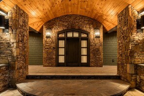 A stone facade with a wooden ceiling, a central door with glass panels, and two wall-mounted lights. - Bear Necessities Lodge: 16,000 SqFt Estate | Indoor Pool, Pickleball, Theater!!! (Sevierville)