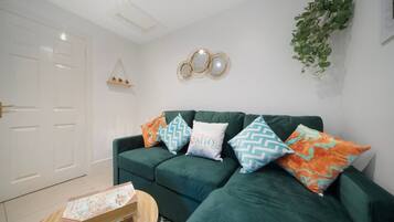 A green sofa with patterned cushions, a wooden coffee table, and a white door.