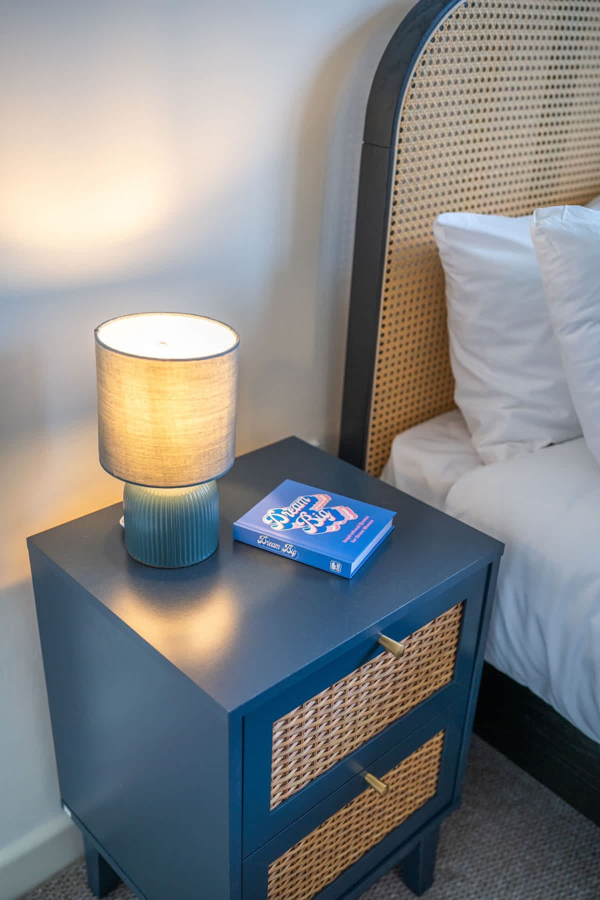 Ein Nachttisch mit Lampe, Buch und einem Korbwäschekorb.