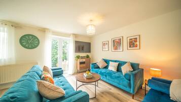 Een woonkamer met een blauwe bank, een ronde salontafel en een klok aan de muur.