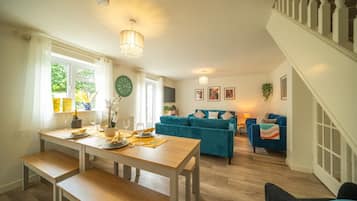 Een eetgedeelte met een houten tafel en banken, een blauwgroene bank en een trap.
