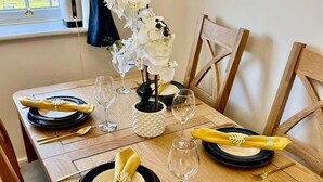 Ein Esstisch ist gedeckt mit Tellern, Besteck und einer Vase mit weißen Blumen.