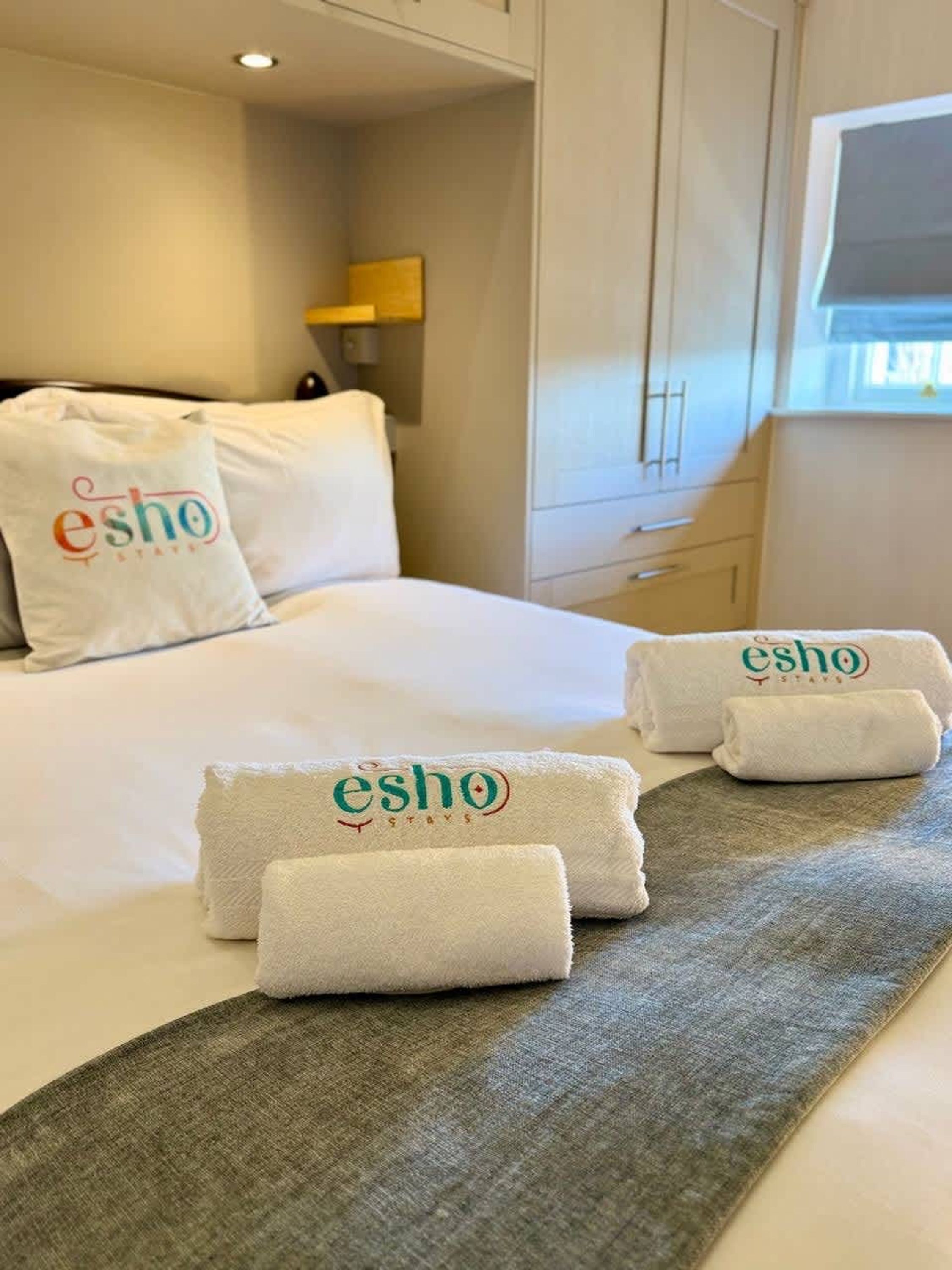 Ein Hotelzimmer mit Bett, Kissen und Handtüchern, verziert mit dem Logo 'esho stays'.