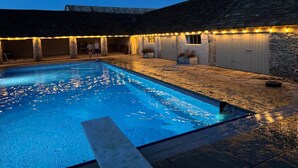 A swimming pool with stone walls and a covered area with string lights. - Stunning Countryside House With Pool and Hot Tub (Malmesbury)