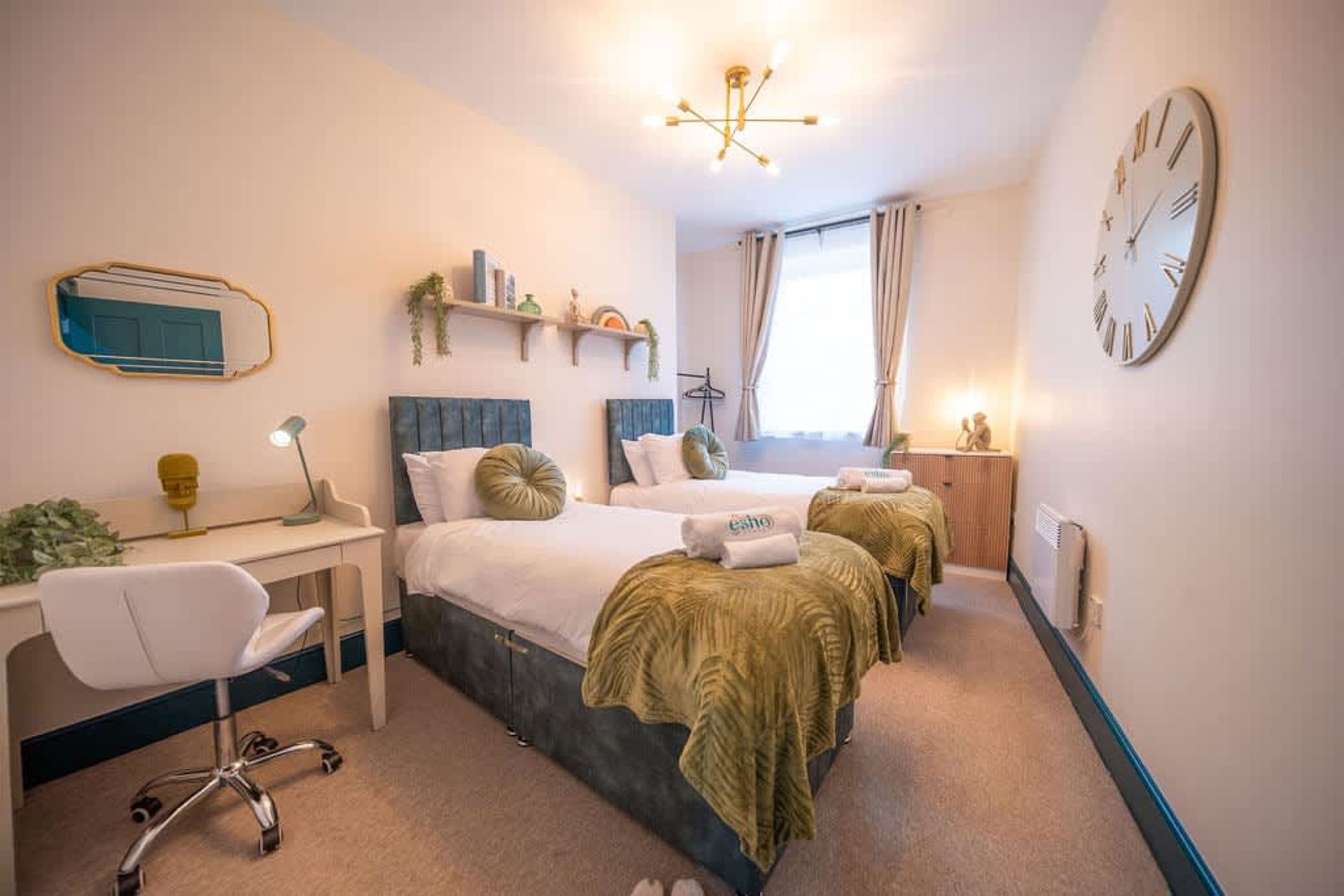 A hotel room with a bed, desk, chair, and a clock on the wall.