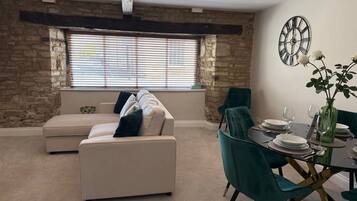 Un salon avec un canapé, des fauteuils turquoise, une table à manger dressée pour quatre personnes et un mur en pierre.