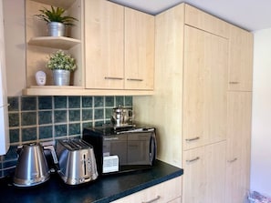 A kitchen with wooden cabinets, a toaster, a kettle, and a microwave on a dark countertop. - Ground Floor Apartment in 18th Century Building (Cirencester)