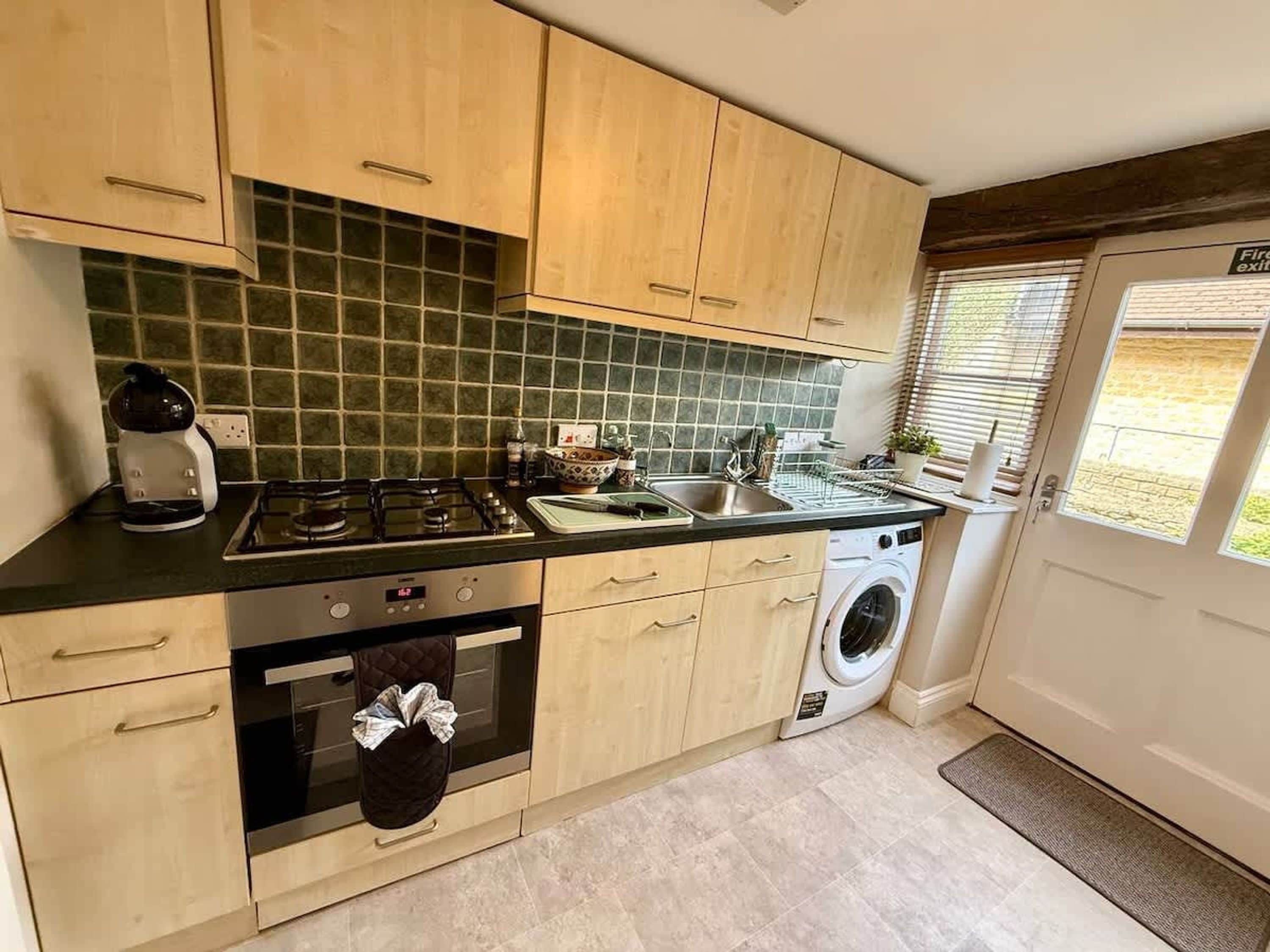 A compact kitchen with a gas stove, oven, microwave, sink, and a washing machine.