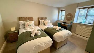 A hotel room with two beds, a desk, a window with blinds, and a radiator.