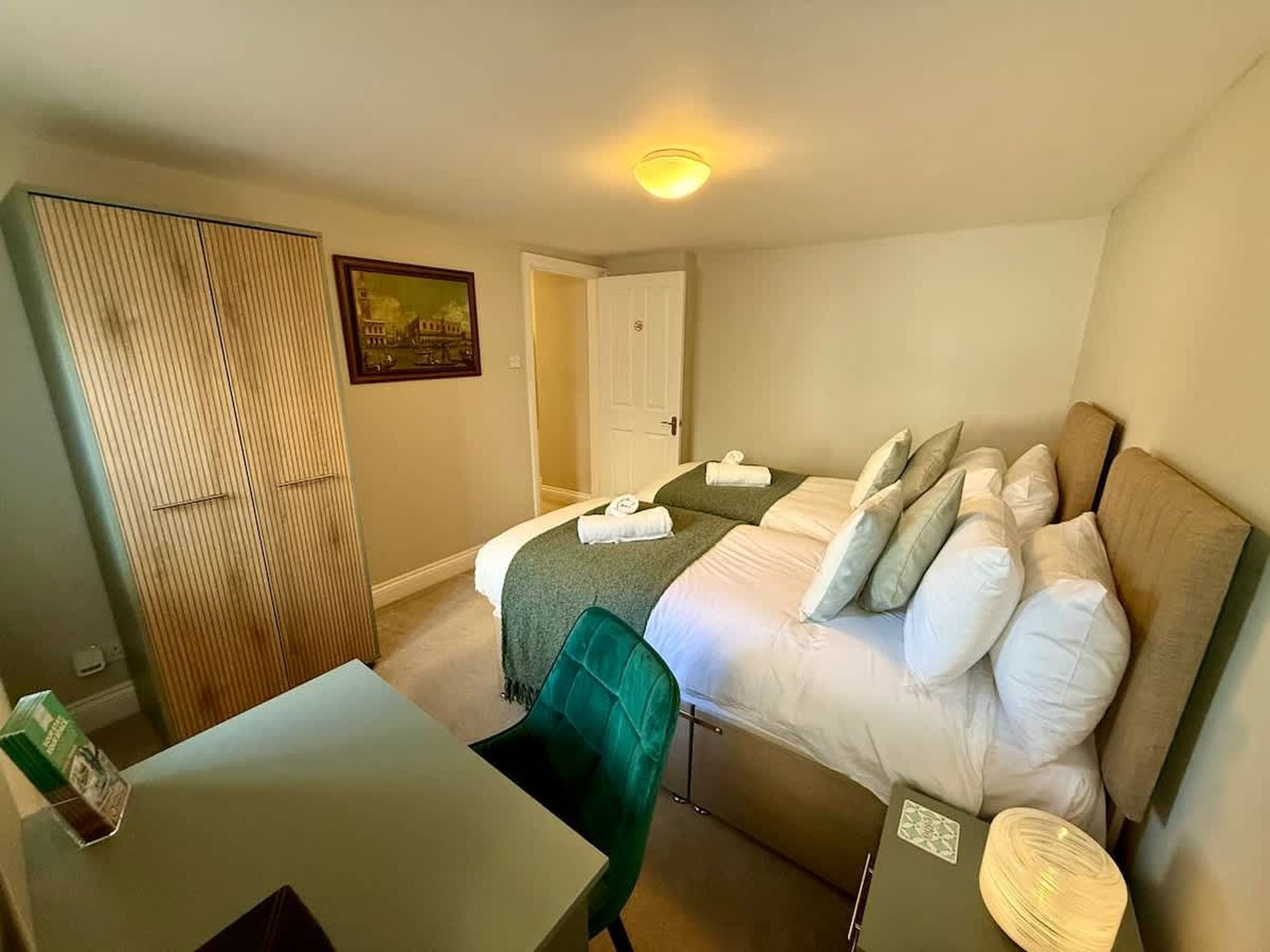 A hotel room with a bed, a desk, a chair, a wardrobe, and a door.