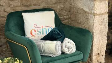A green armchair with a white pillow, a small round table with a leaf pattern, and a stone wall.