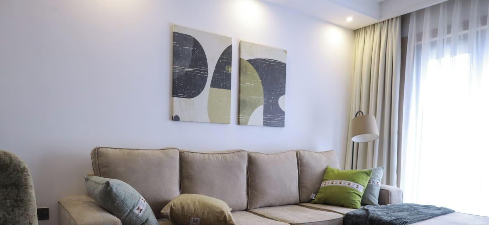 A living room with a beige sofa, two cushions, and abstract wall art.