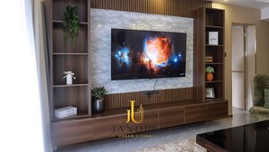 Un salón con un televisor de pantalla plana grande montado en una pared, estanterías de madera con objetos decorativos y un salpicadero tipo mármol.