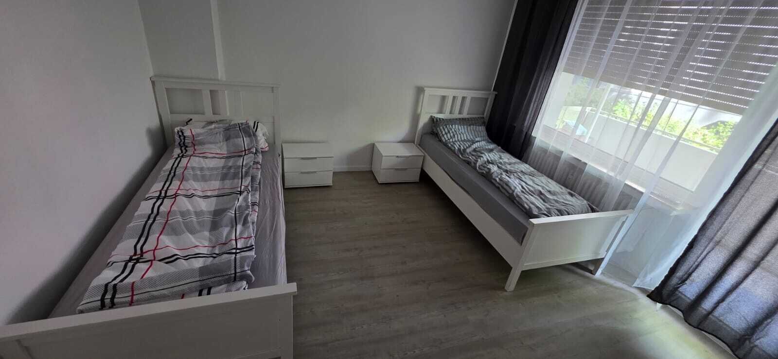 Een slaapkamer met twee enkele bedden, een bankje en een raam met gordijnen.