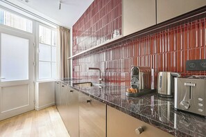 A modern kitchen with a marble countertop, stainless steel appliances, and a red-tiled backsplash. - Luxury Duplex Saint-Germain Notre Dame (Paris)