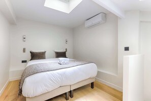A bedroom with a bed, a skylight, an air conditioning unit, and a wooden floor. - Luxury Duplex Saint-Germain Notre Dame (Paris)