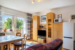 A compact living space with a dining area, a sofa, a TV, a microwave, and a refrigerator.
