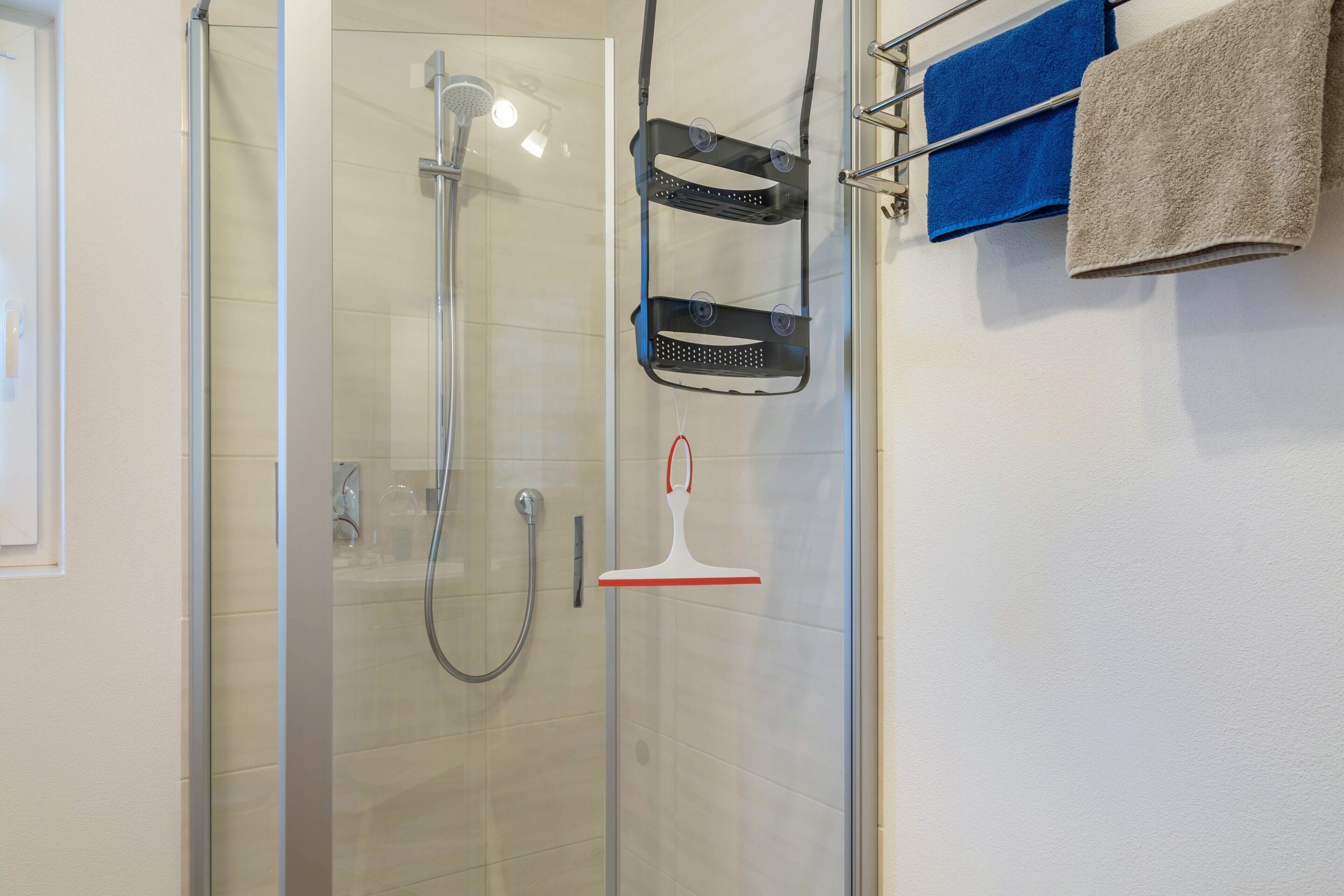 Ein Duschbereich mit Glasabtrennung, Handbrause und einem Handtuchhalter mit Handtüchern.