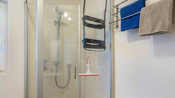 Ein Duschbereich mit Glasabtrennung, Handbrause und einem Handtuchhalter mit Handtüchern.